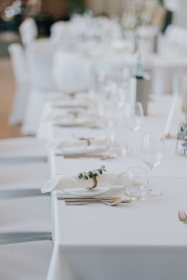 Festlich gedeckter Tisch mit weißer Tischdecke, weißen Servietten mit Blätterschmuck und eleganten Weingläsern