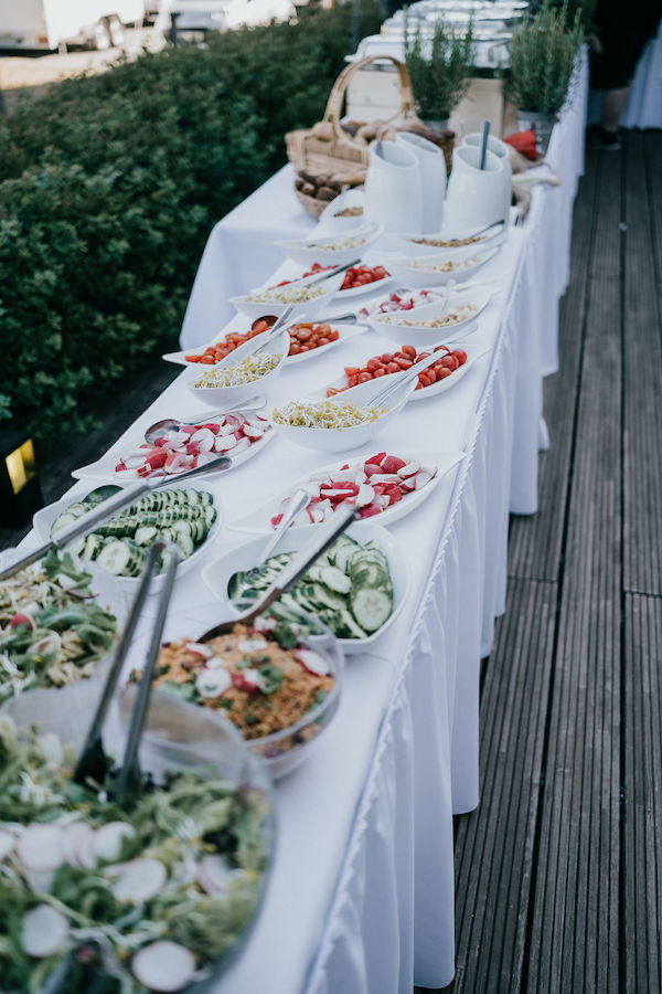 Buffettisch mit weißer Tischdecke und verschiedenen Schälchen mit Gemüse und Salaten