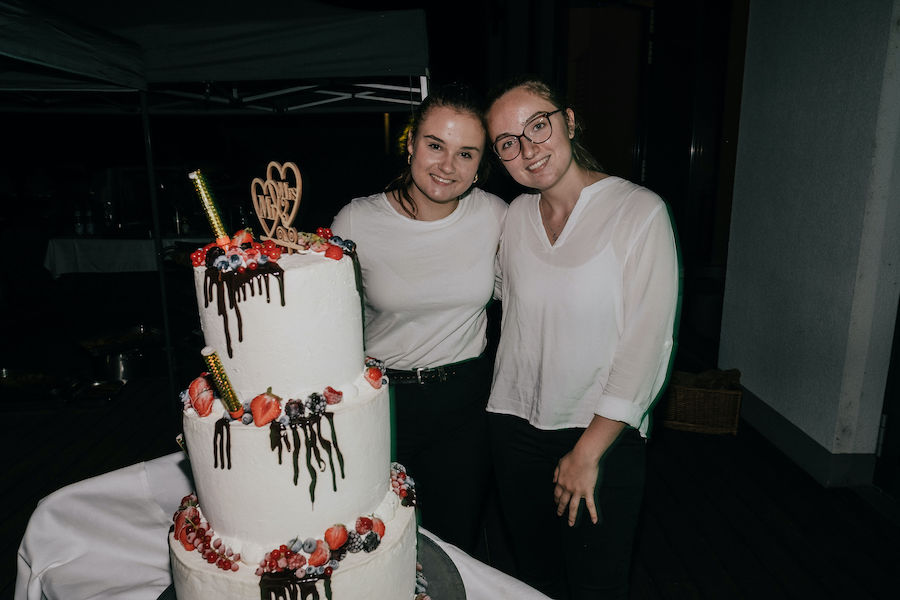 Zwei Damen vom Cateringpersonal, stehend neben einer dreischichtigen Hochzeitszorte